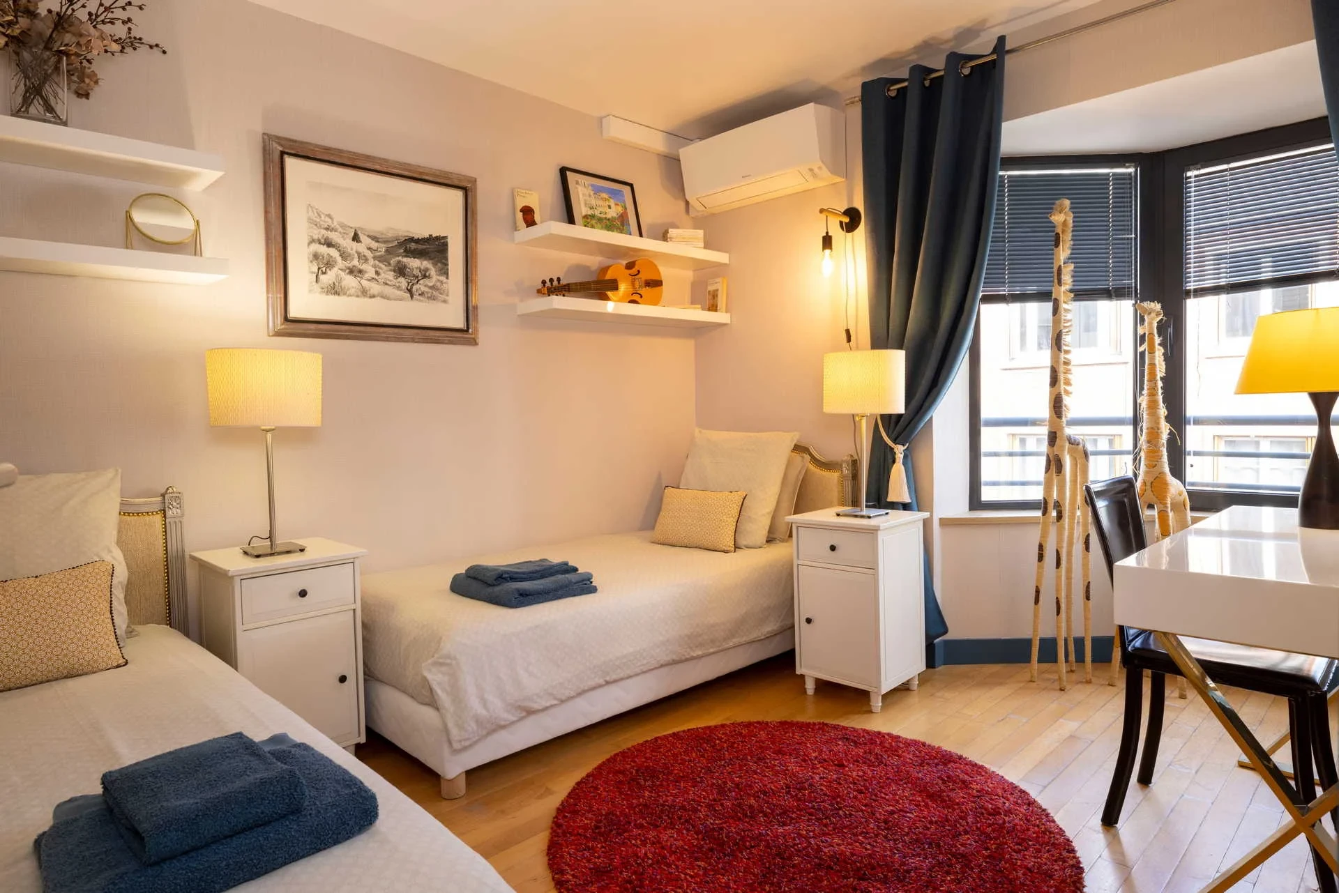 Chambre à deux lits de MAISON LAVAUD - Paris, avec serviettes bleues pliées sur les lits et grande fenêtre à stores.