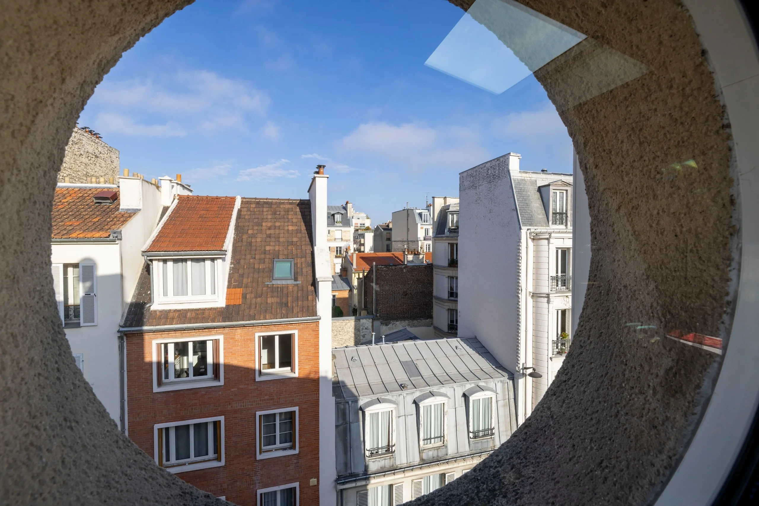 Toits parisiens vus à travers une fenêtre ronde de MAISON LAVAUD - Paris, résidence hôtelière de luxe à Paris.