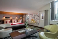 Chambre avec lit double, coin salon et dalles de verre intégrées au sol, sous un plafond incliné.