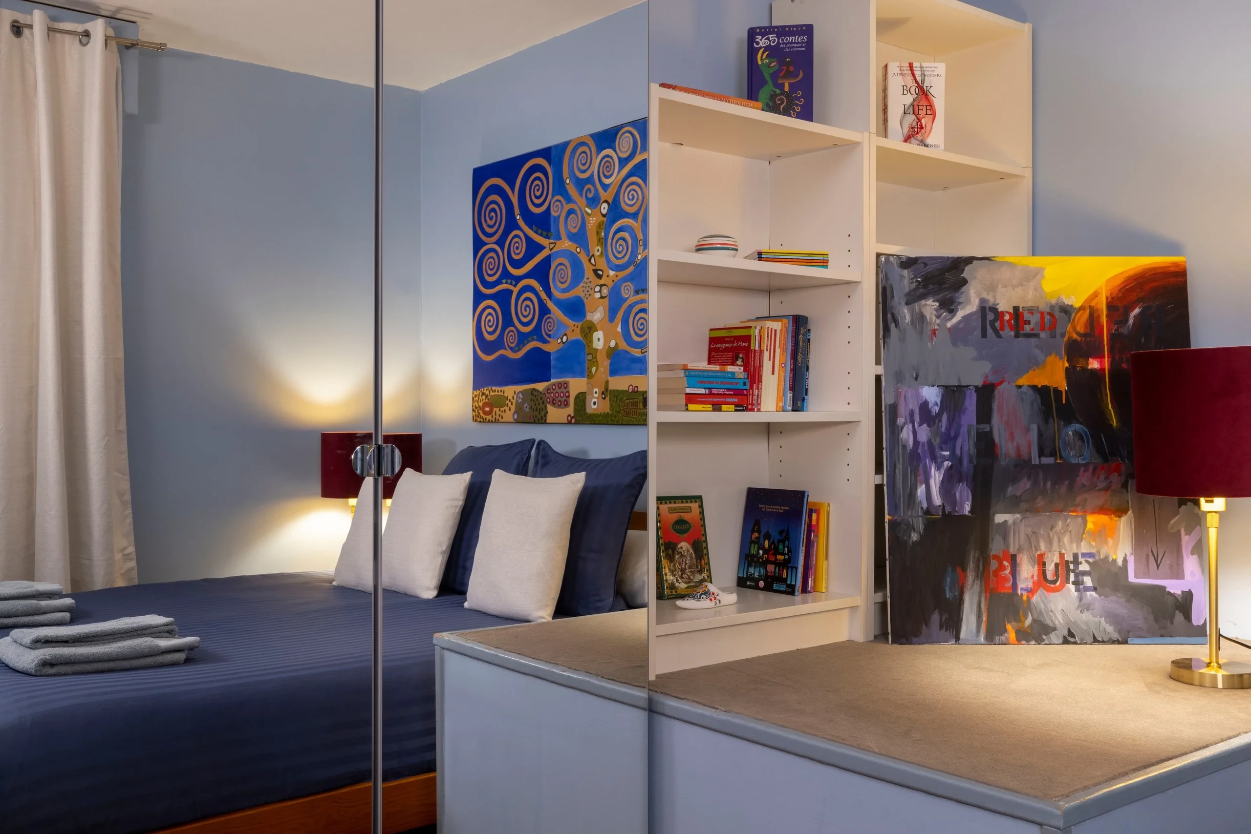 Chambre de la résidence hôtelière de luxe MAISON LAVAUD - Paris, avec lit bleu, bibliothèque et tableaux colorés.