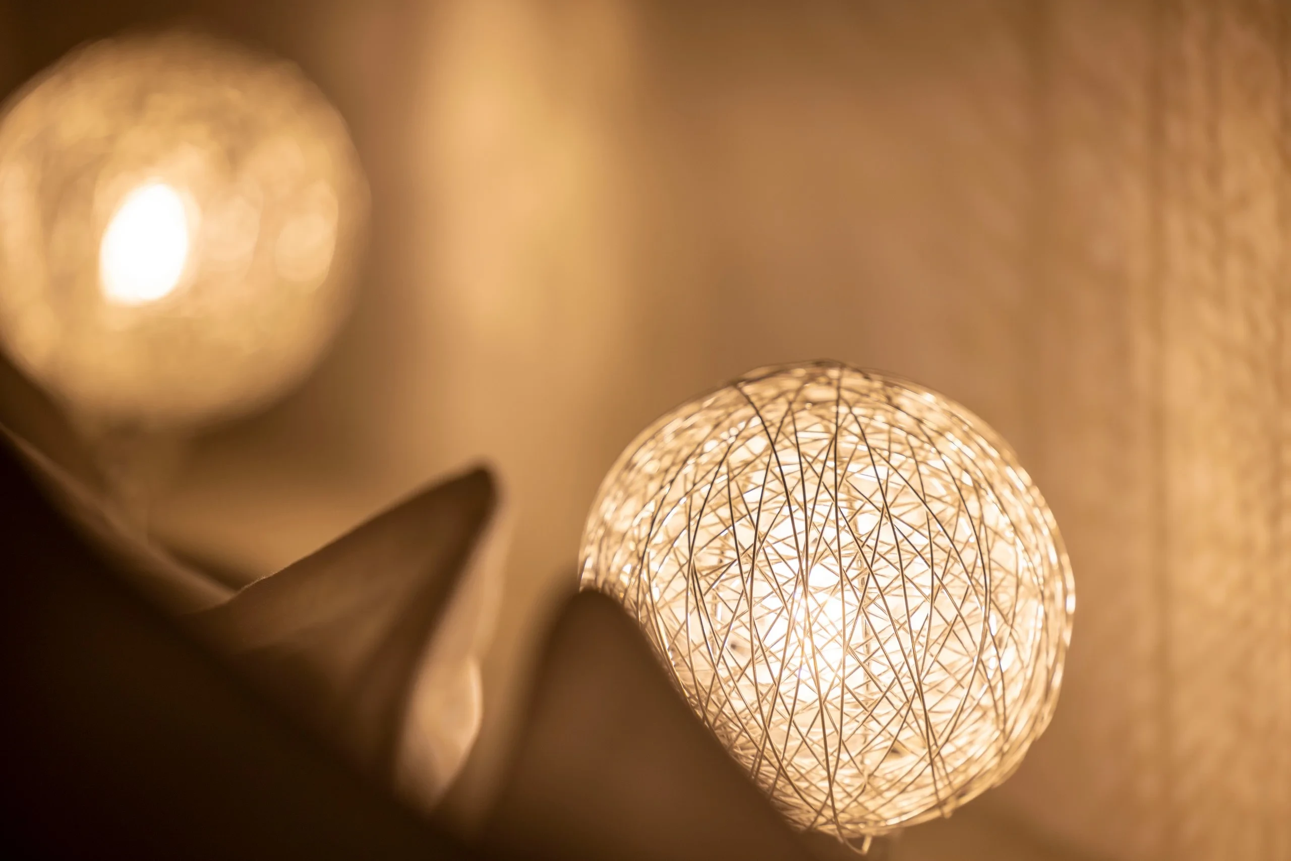Gros plan sur l’abat-jour sphérique aux fils entrecroisés d’une lampe allumée.