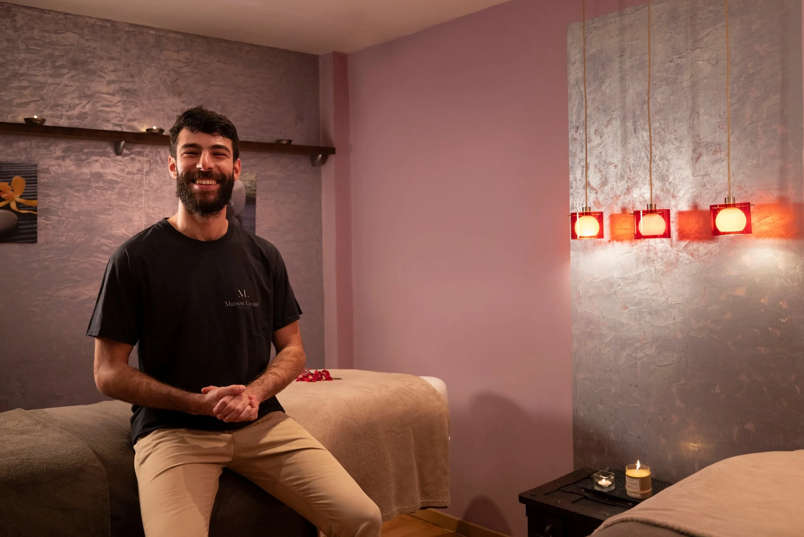 Un homme souriant, les mains jointes, assis au bord d’une table de massage.