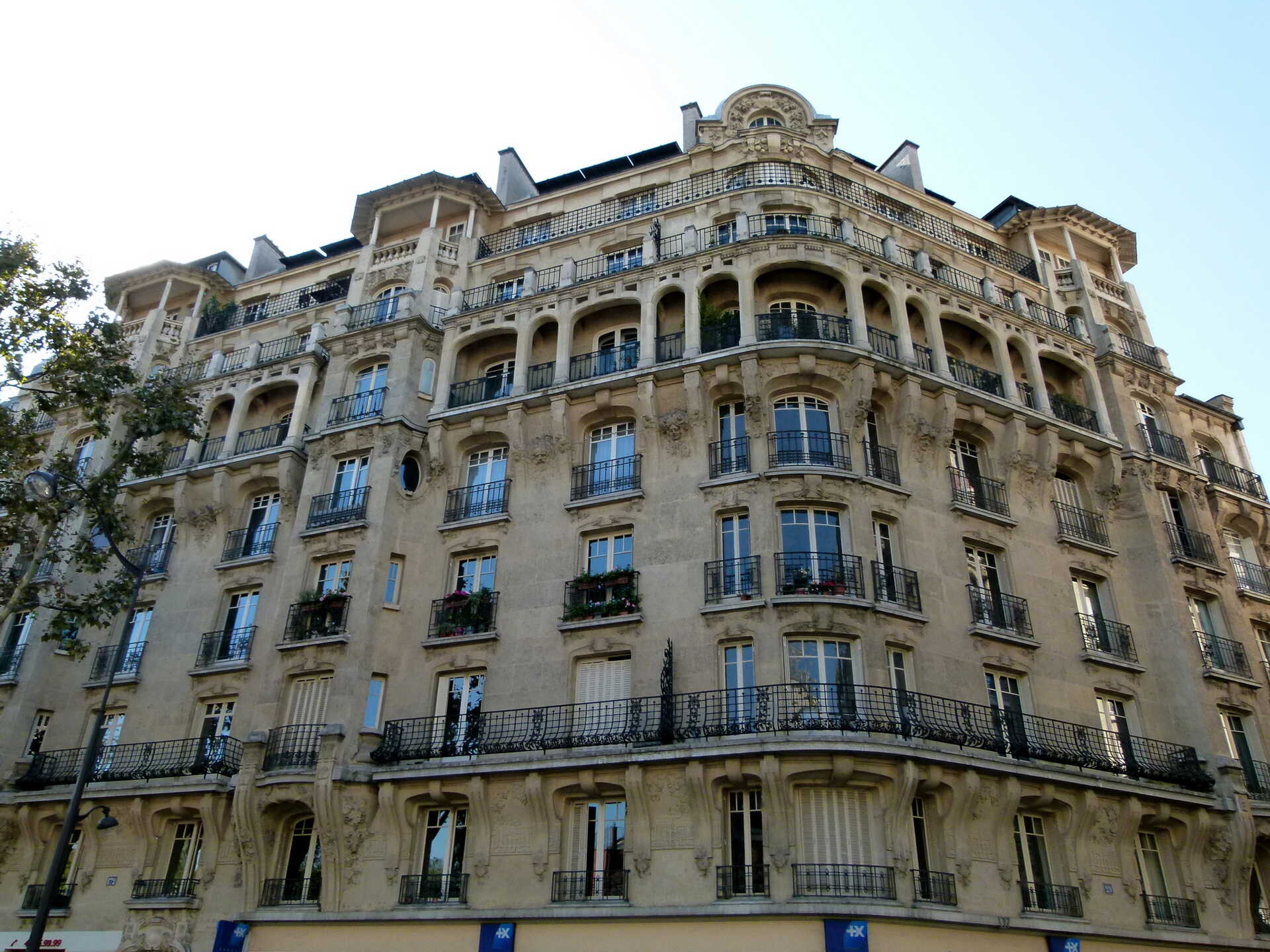 Immeuble d’angle en pierre sculptée, avec balcons en ferronnerie et loggias à arcades.