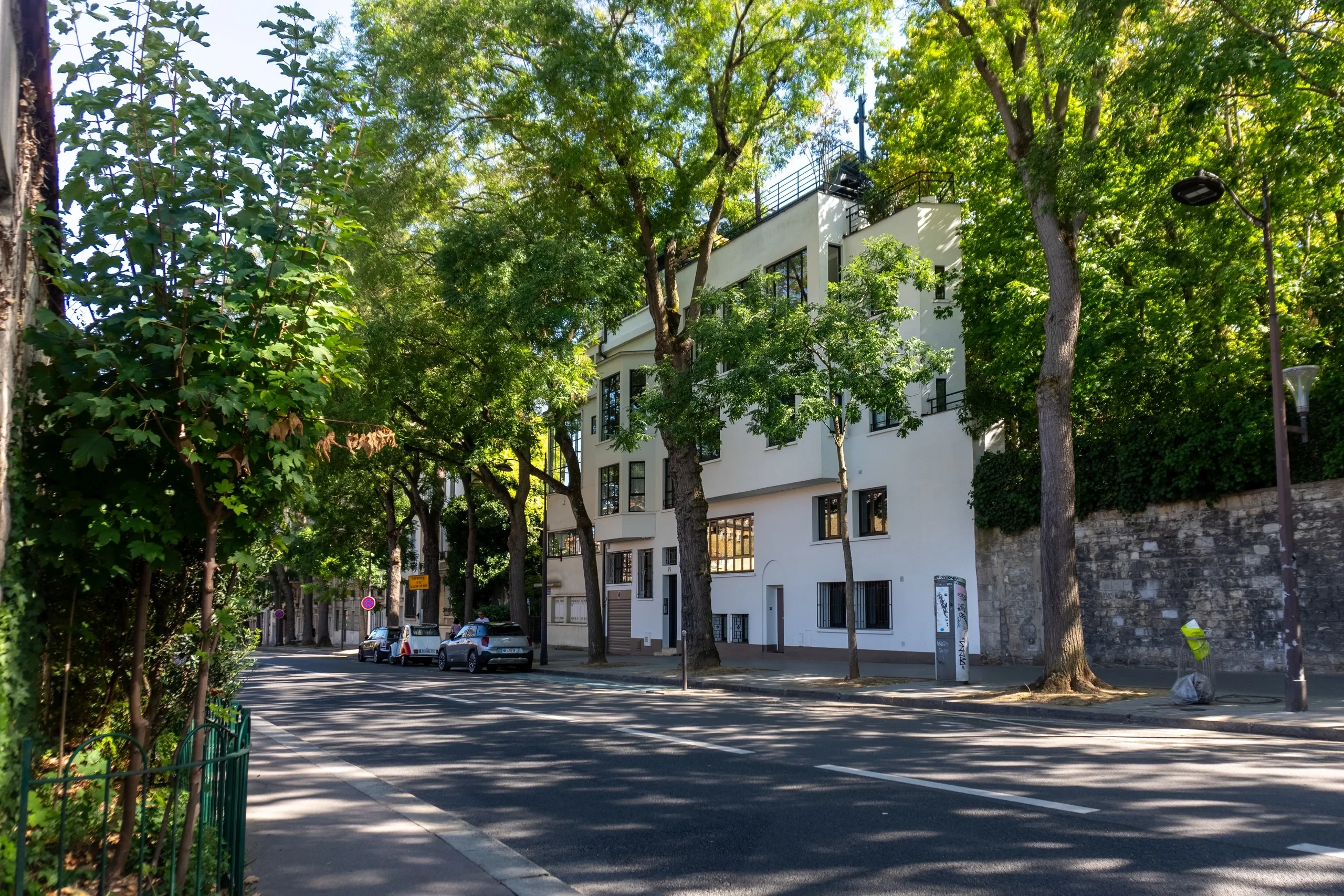 Bâtiment blanc aux grandes fenêtres dans une rue bordée d’arbres.