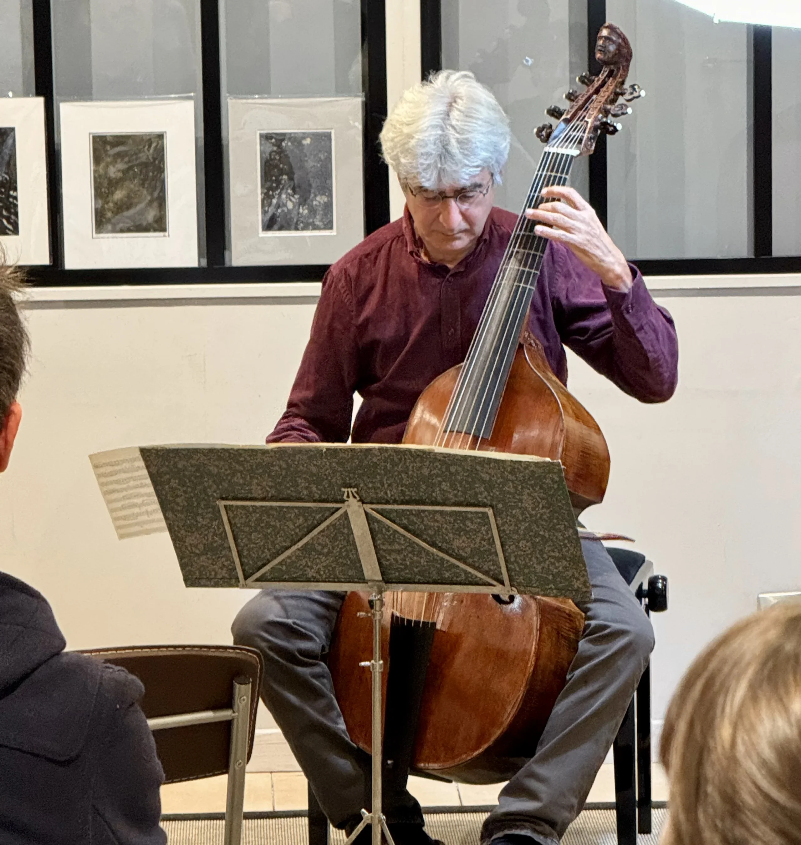 Un musicien joue de la viole de gambe devant un pupitre et un public.
