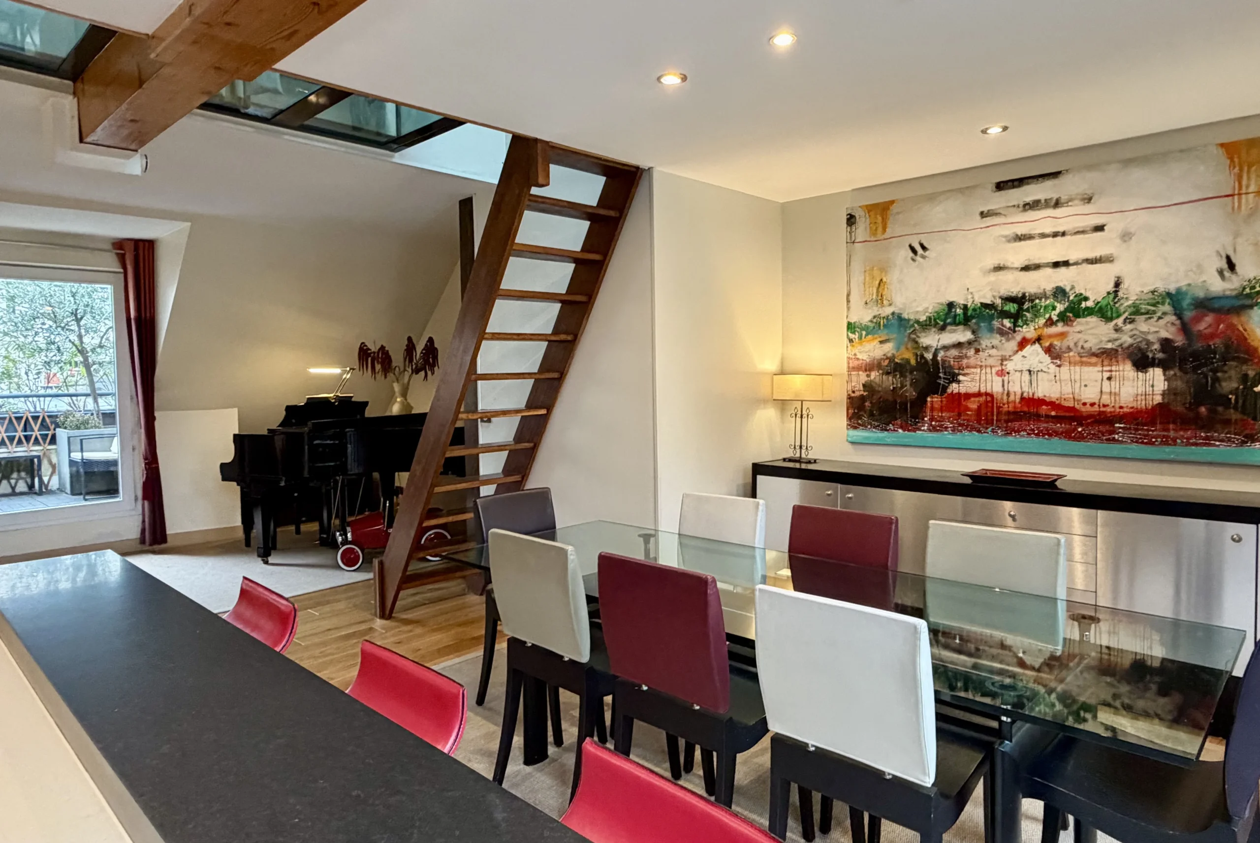 Salle à manger de MAISON LAVAUD - Paris avec table en verre, piano et escalier en bois.