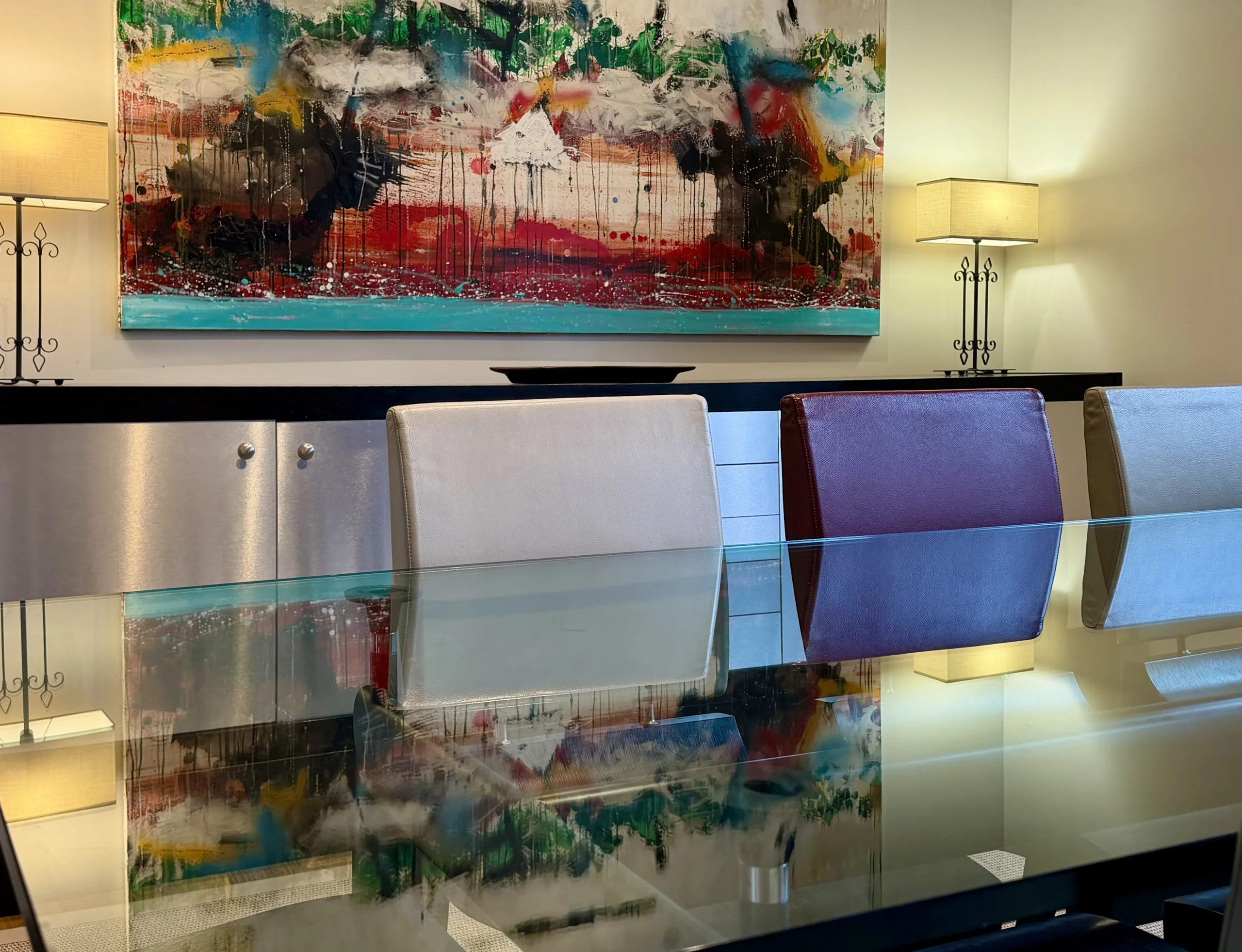 Table en verre reflétant une grande peinture abstraite multicolore dans un appart hôtel de luxe à Paris.