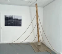 Installation composée d’un haut poteau en bois sur un socle en béton, avec plusieurs cordes retombant au sol.