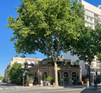 Façade en brique du café-restaurant Poinçon, avec de grandes fenêtres cintrées sous les arbres.