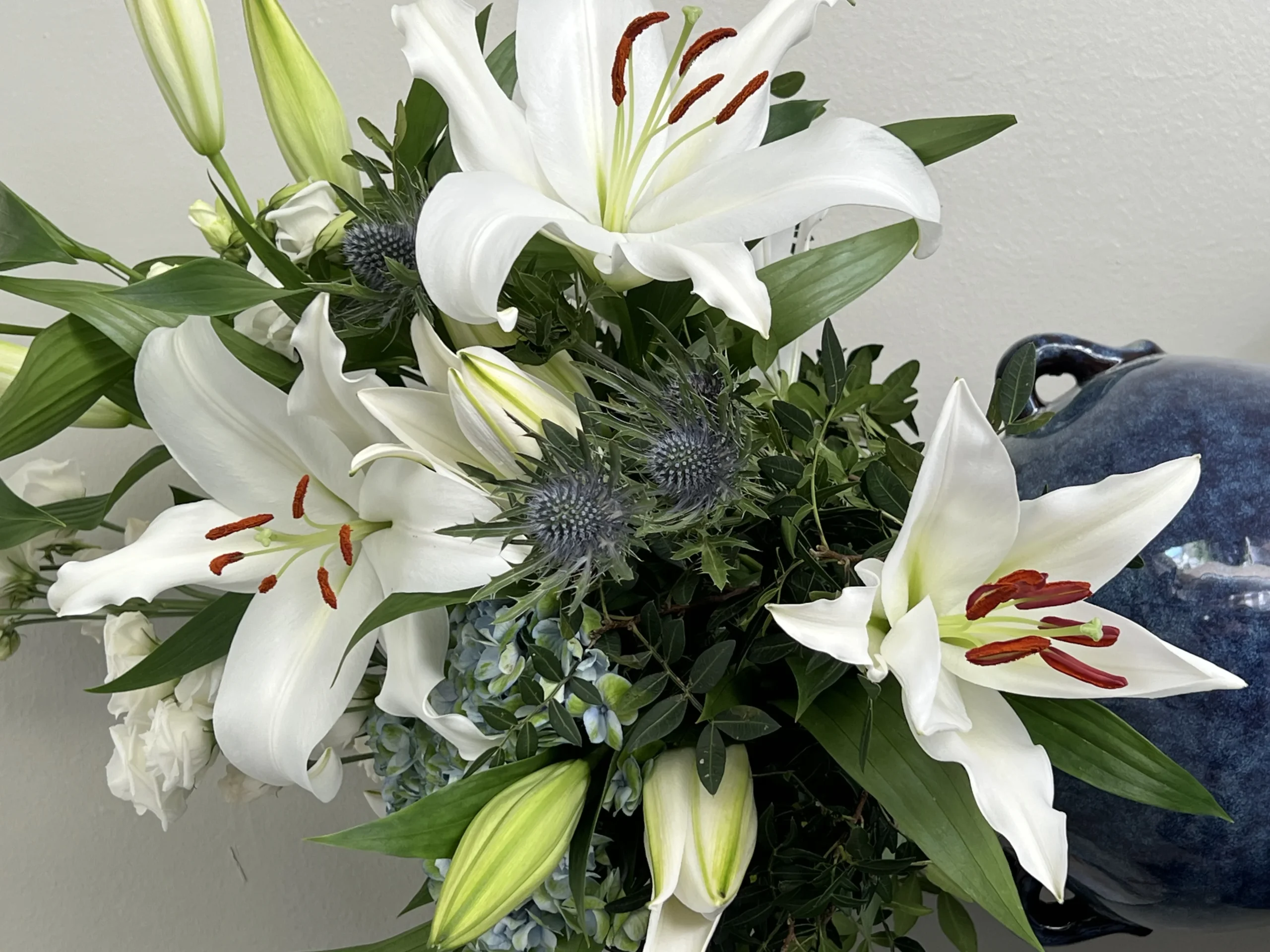 Bouquet de lys blancs et de chardons bleutés près d’une céramique bleue.