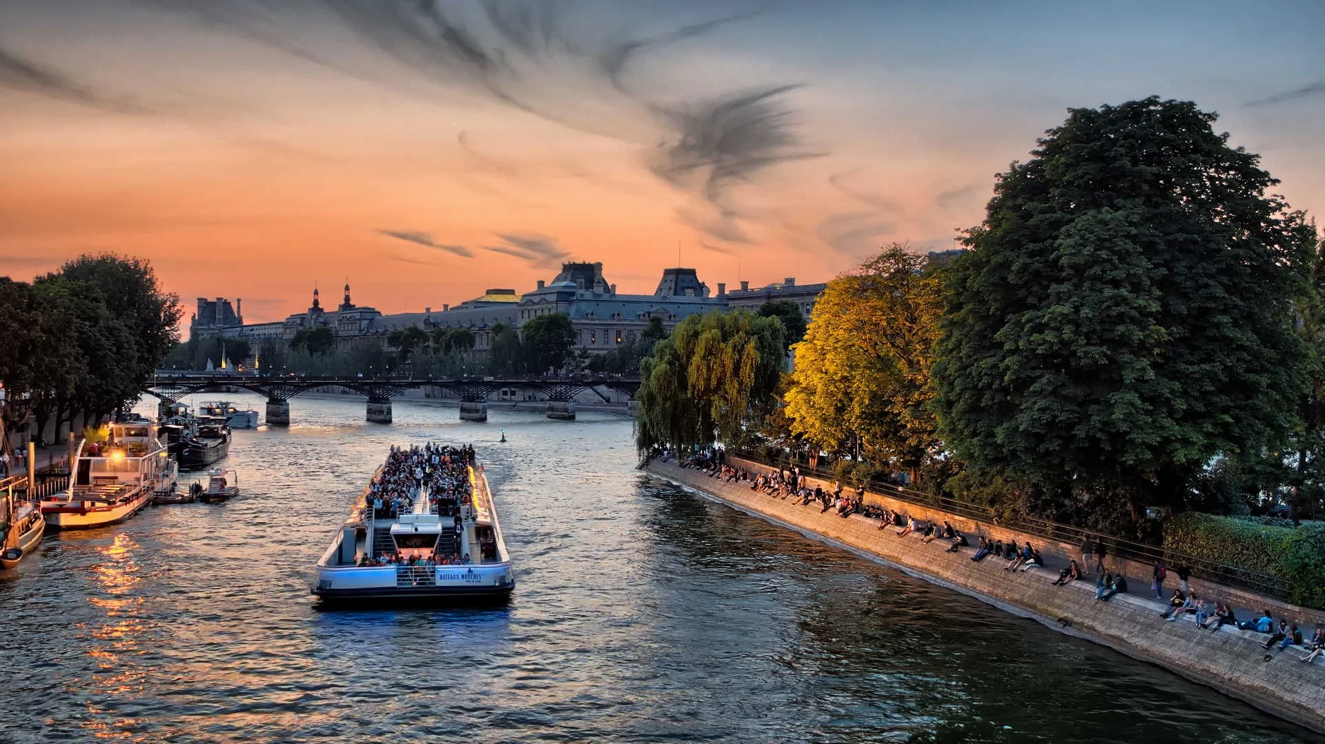 Un bateau de promenade sur la Seine à Paris au crépuscule, entre des quais arborés.