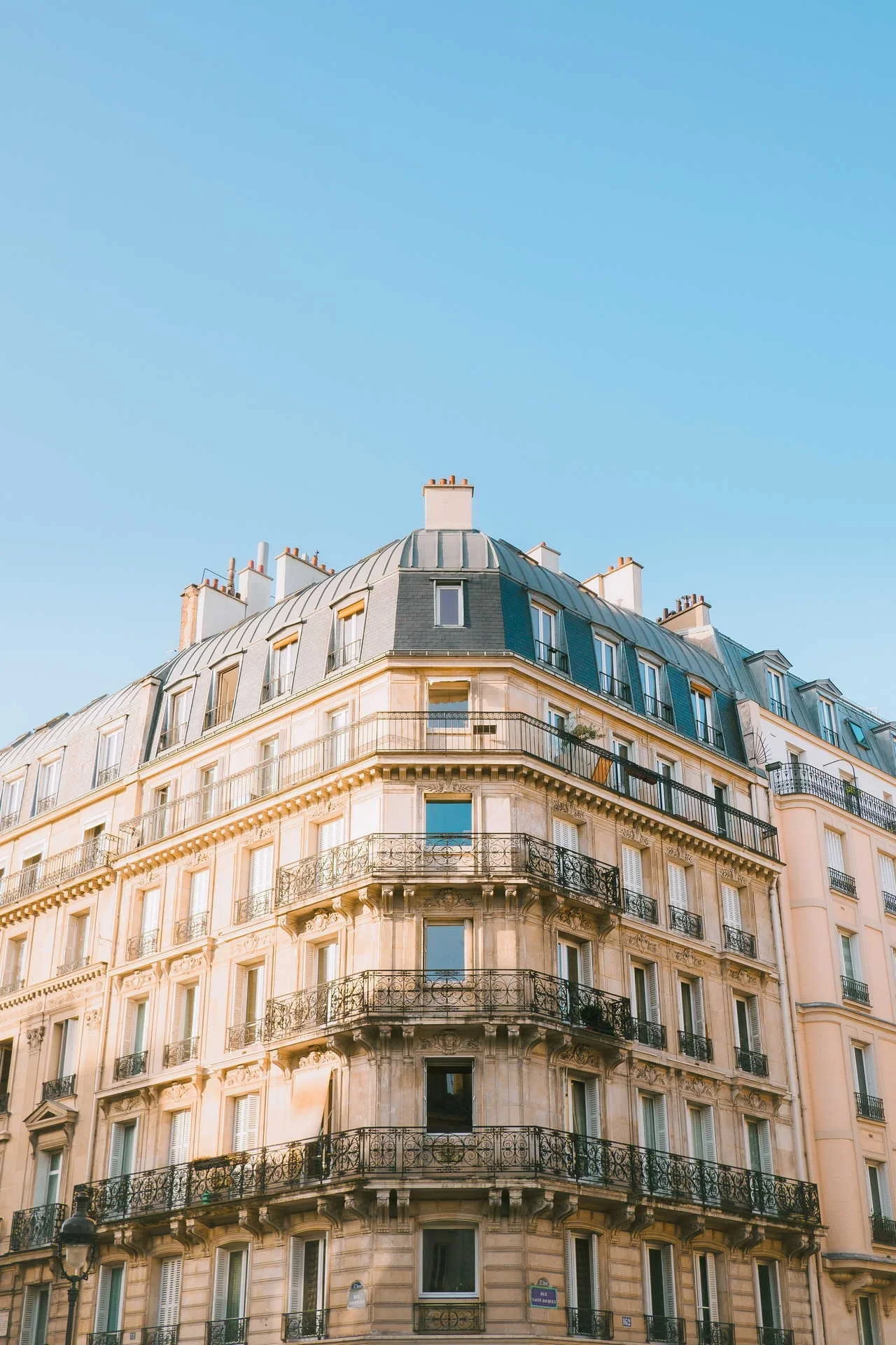 Façade d’angle d’un immeuble haussmannien, avec balcons en fer forgé et toiture mansardée.